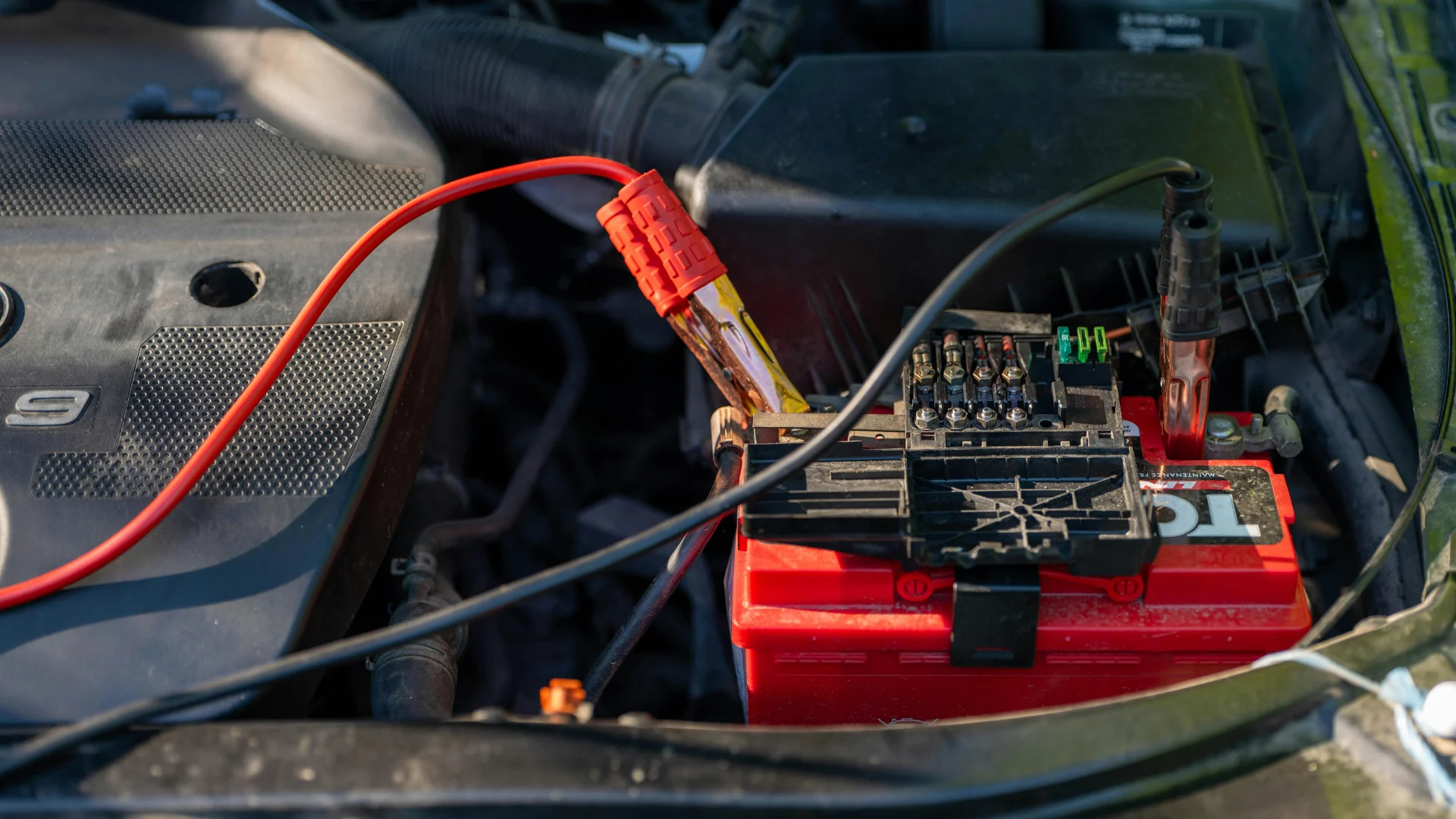 Red and black jumper cables connected to the terminals of a red automotive vehicle battery, representing energy storage components that utilize conductive carbon materials.