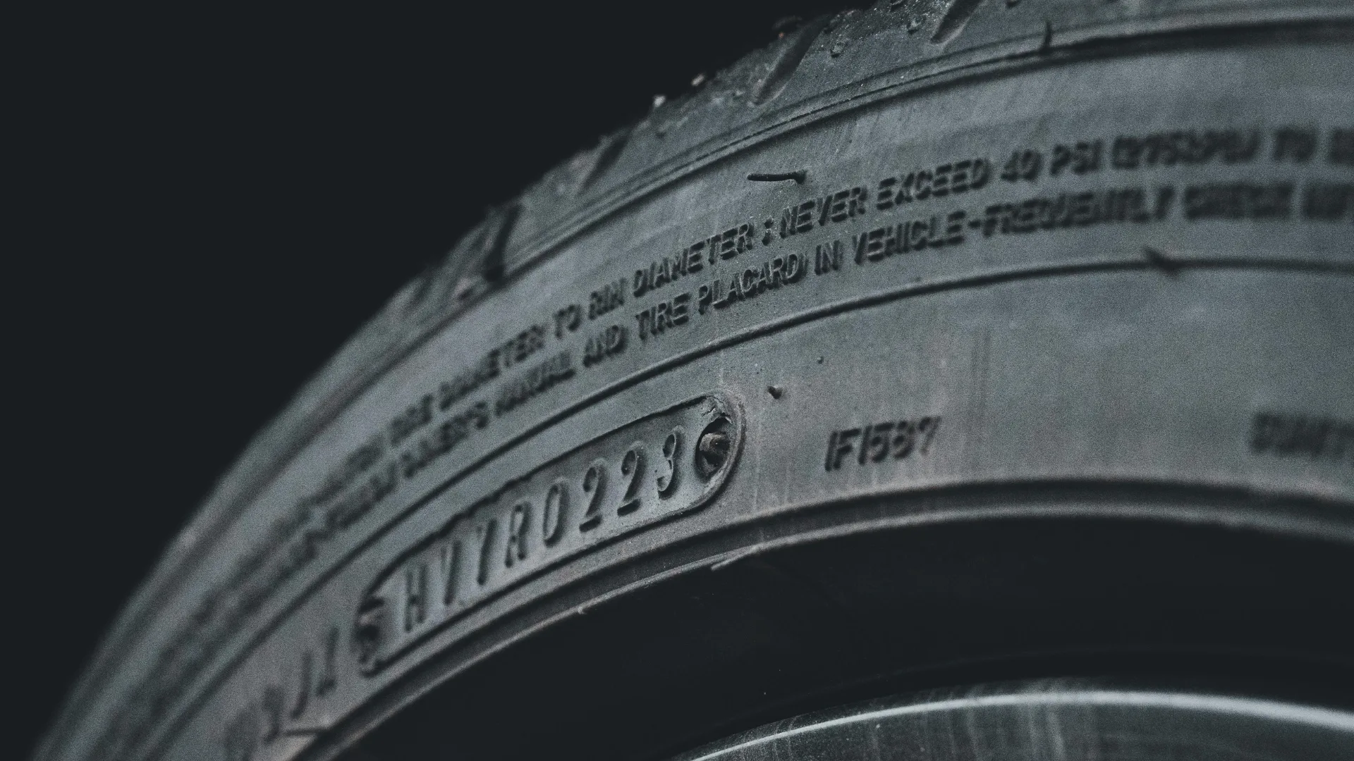 Extreme close-up of a rubber automotive vehicle tire sidewall highlighting the tread depth and material texture, manufactured using carbon black reinforcement.