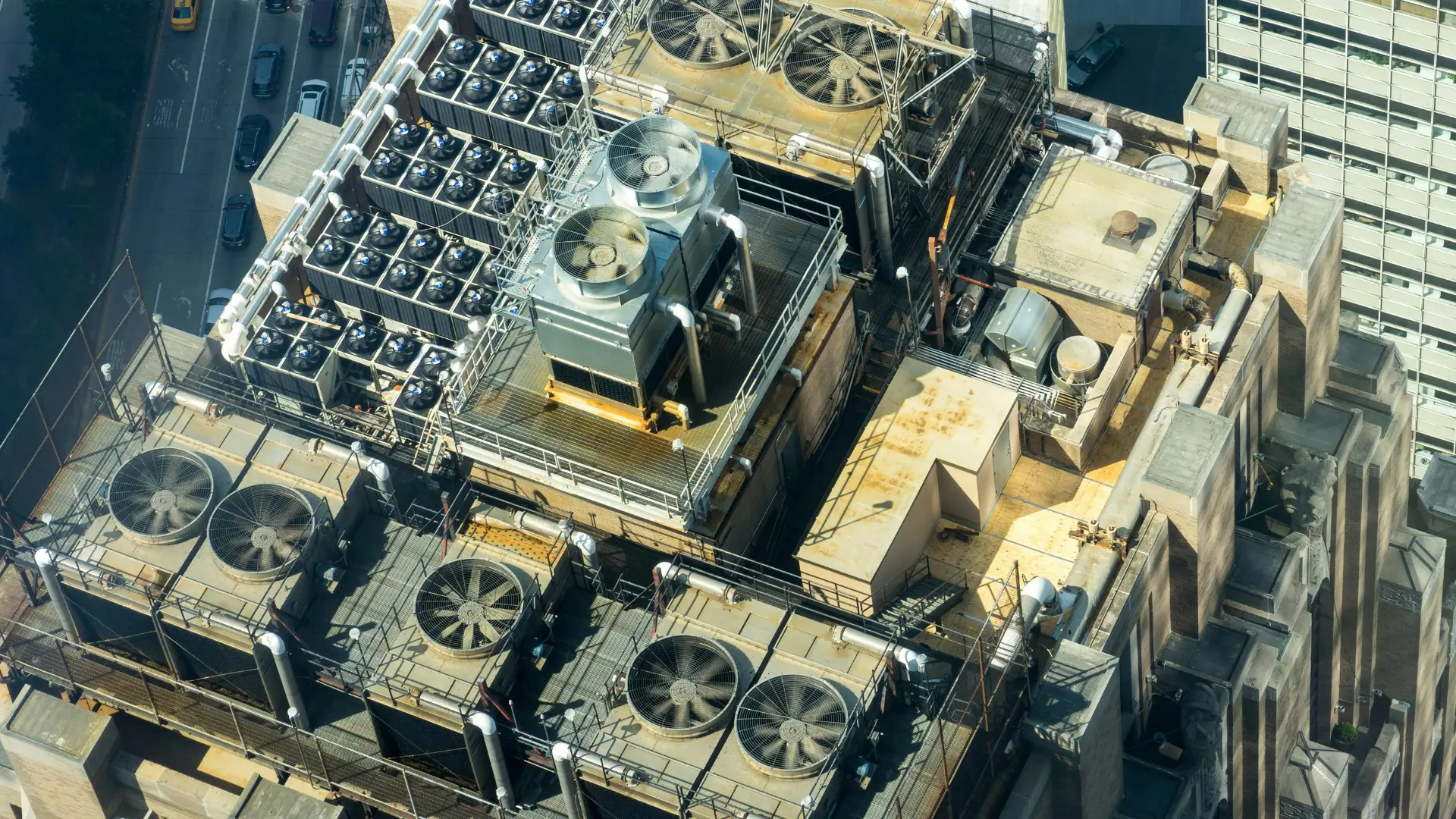 Aerial view of heavy-duty commercial HVAC systems, industrial cooling towers, and large ventilation fans requiring air filtration on a city building rooftop.
