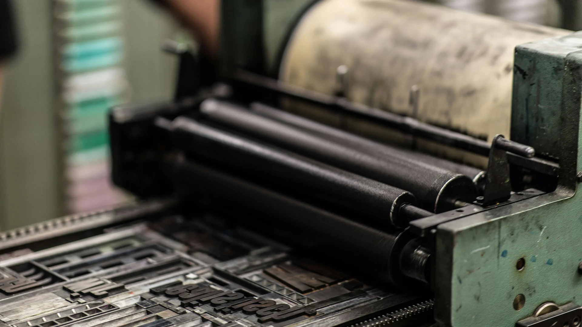 Close-up of a traditional letterpress printing machine featuring heavy metal type plates and rubber rollers coated in deep carbon black printing ink.