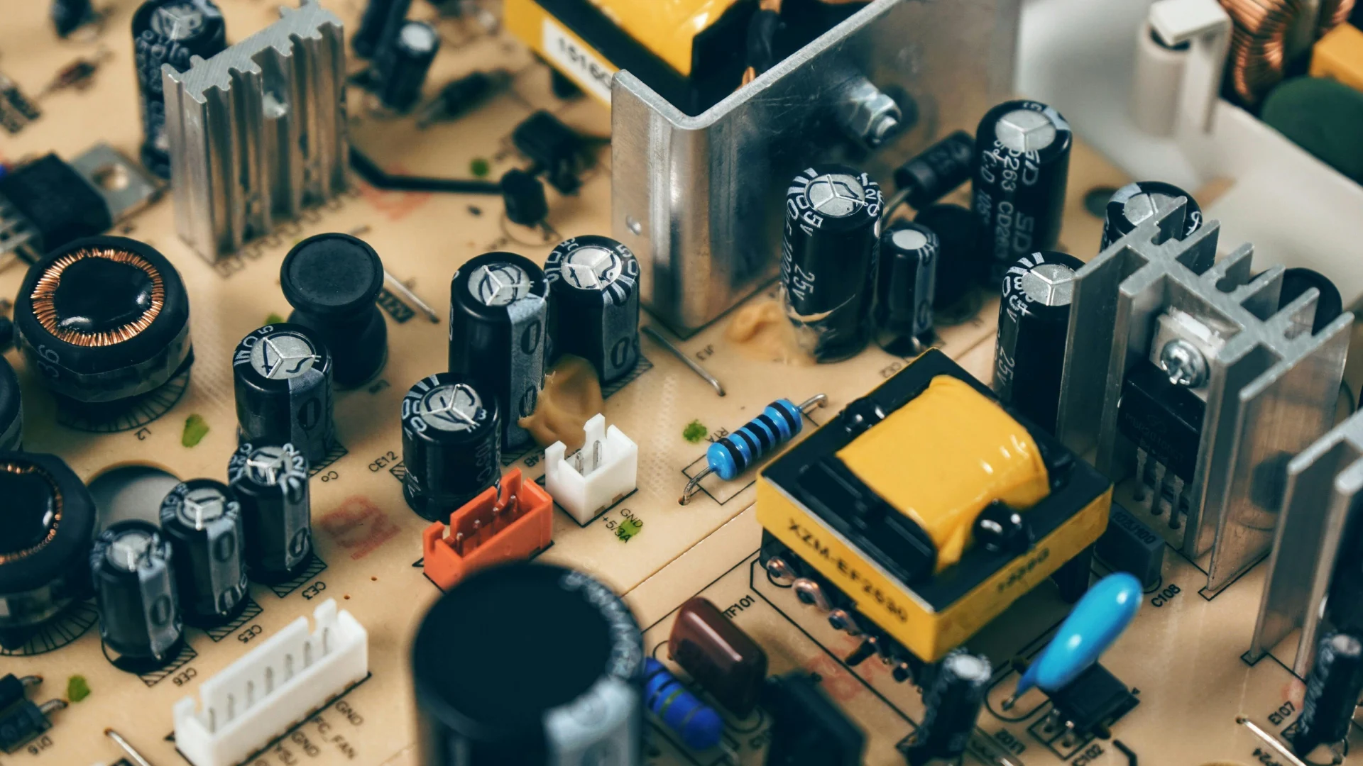 Macro photograph of a complex electronic printed circuit board (PCB) featuring black capacitors, resistors, and transformers that rely on specialized conductive components.