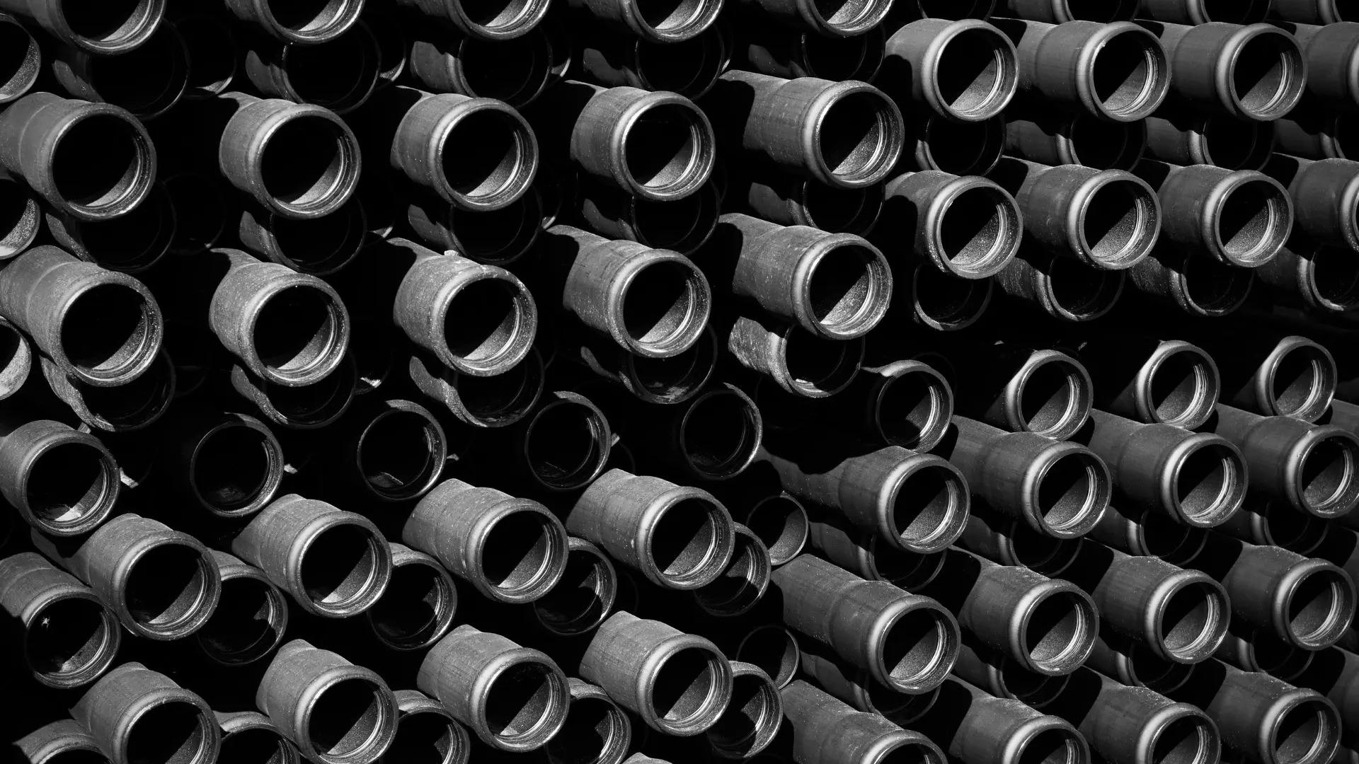 Neatly stacked rows of manufactured black plastic industrial pipes, which utilize specialized carbon black compounds for critical UV resistance and structural durability.