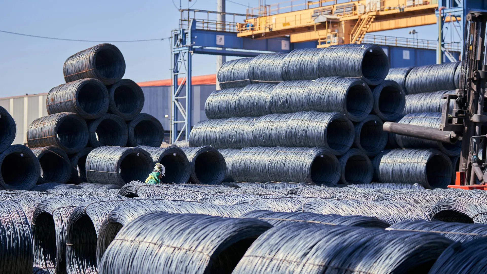 Massive coils of heavy industrial steel wire stacked tightly together in a large outdoor manufacturing yard, awaiting further processing and protective industrial coatings.