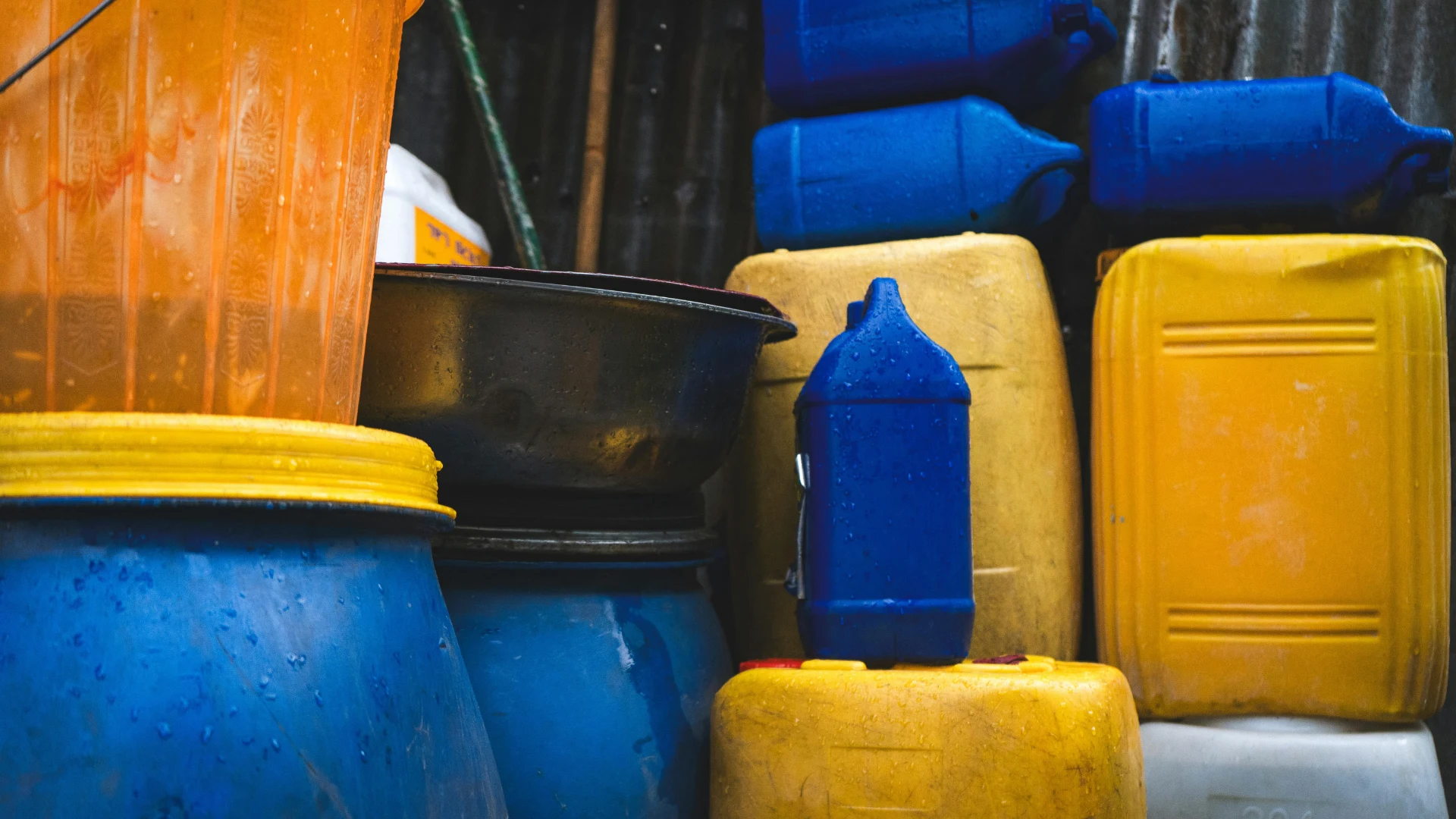 A stack of heavy-duty blue and yellow high-density polyethylene (HDPE) plastic drums and jerrycans used for bulk industrial chemical liquid storage.