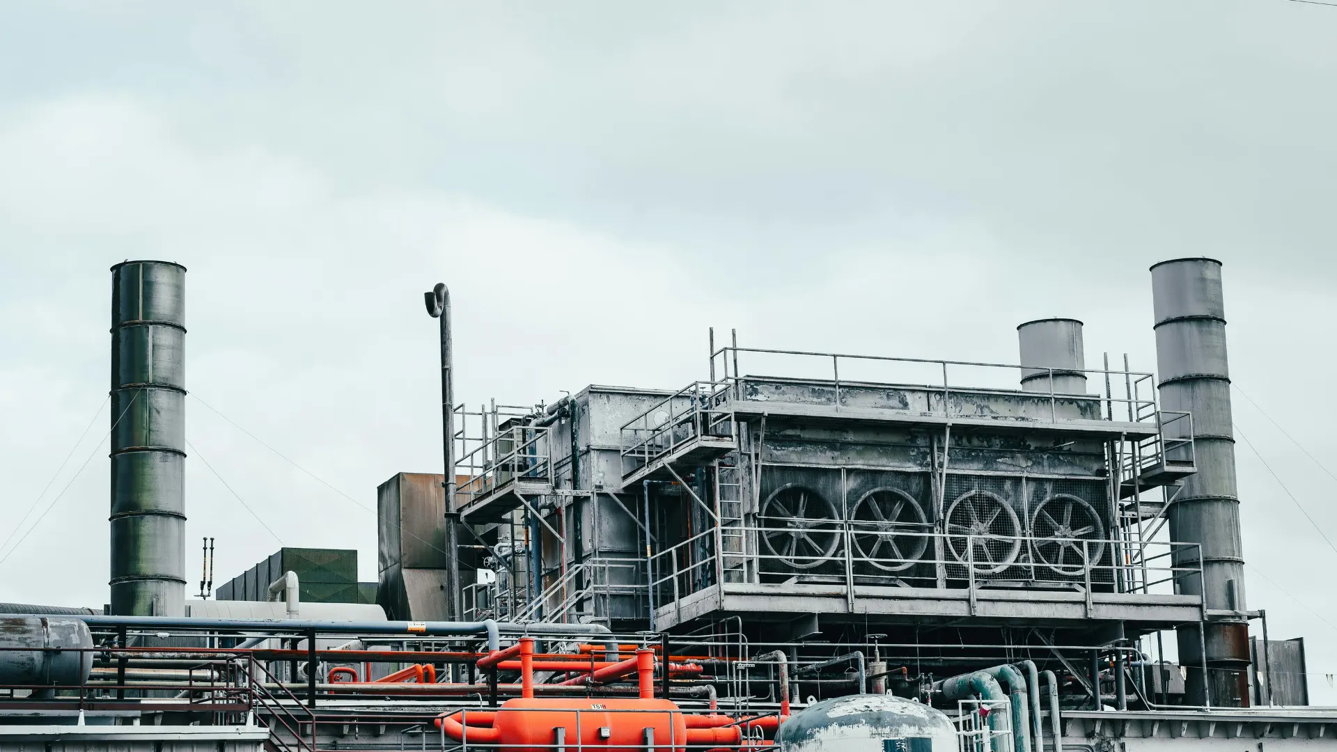 Close-up view of heavy industrial rooftop machinery, featuring large ventilation exhaust fans and complex metal piping networks for air management.