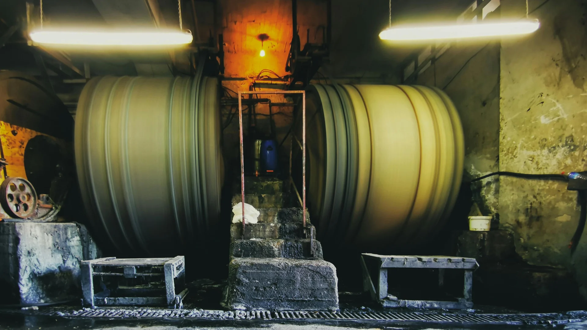 Large, heavy-duty industrial rotary mixing drums in rapid motion within a dimly lit processing plant, utilized for material processing and chemical compounding.