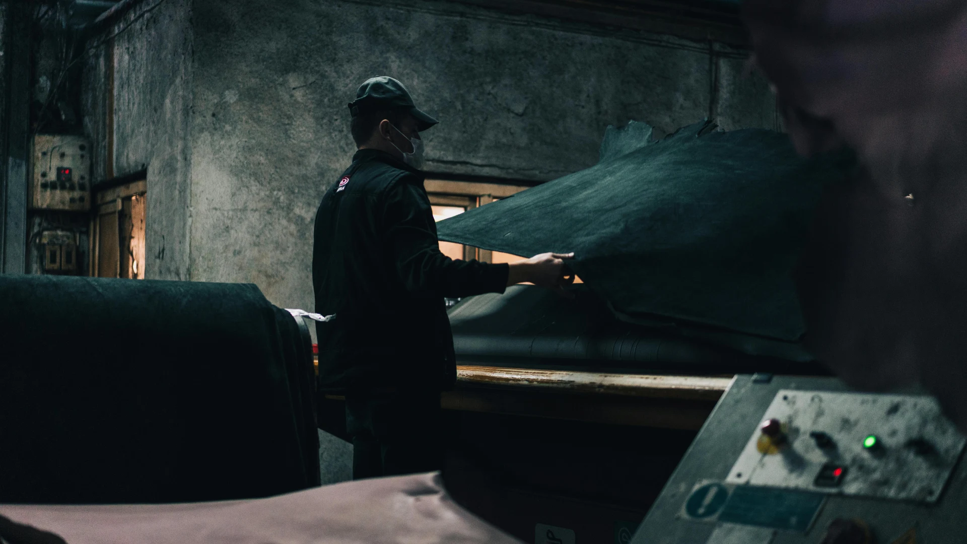 A factory worker handling a large, thick sheet of industrial black rubber, a material that relies heavily on carbon black reinforcement for enhanced durability and strength.