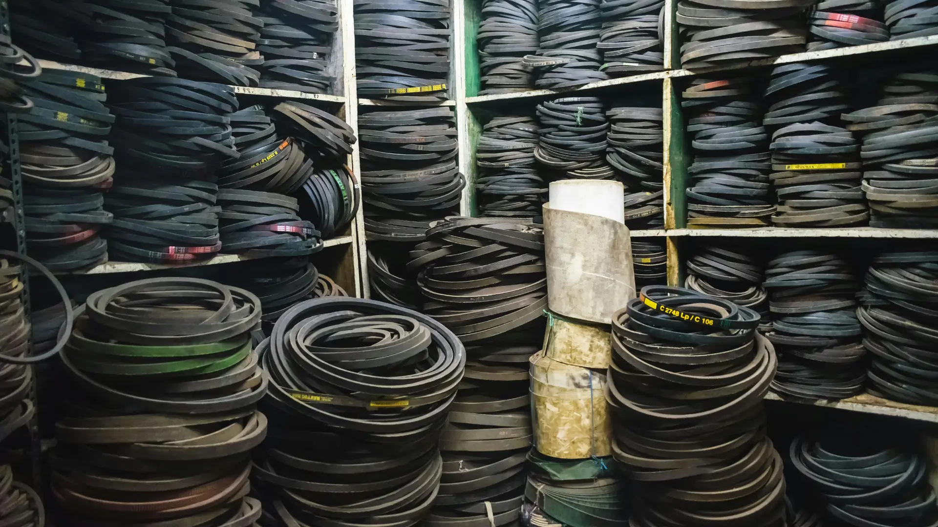 A dense warehouse storage room packed floor-to-ceiling with heavy-duty black industrial rubber V-belts, which rely extensively on carbon black for tensile strength and heat resistance.