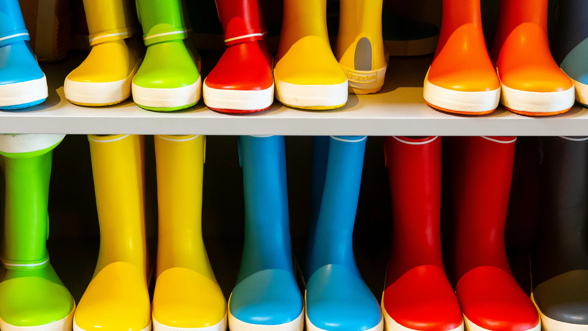 Multiple rows of brightly colored manufactured rubber rain boots lined up on storage shelves, representing commercial rubber compounding and variable pigment applications.