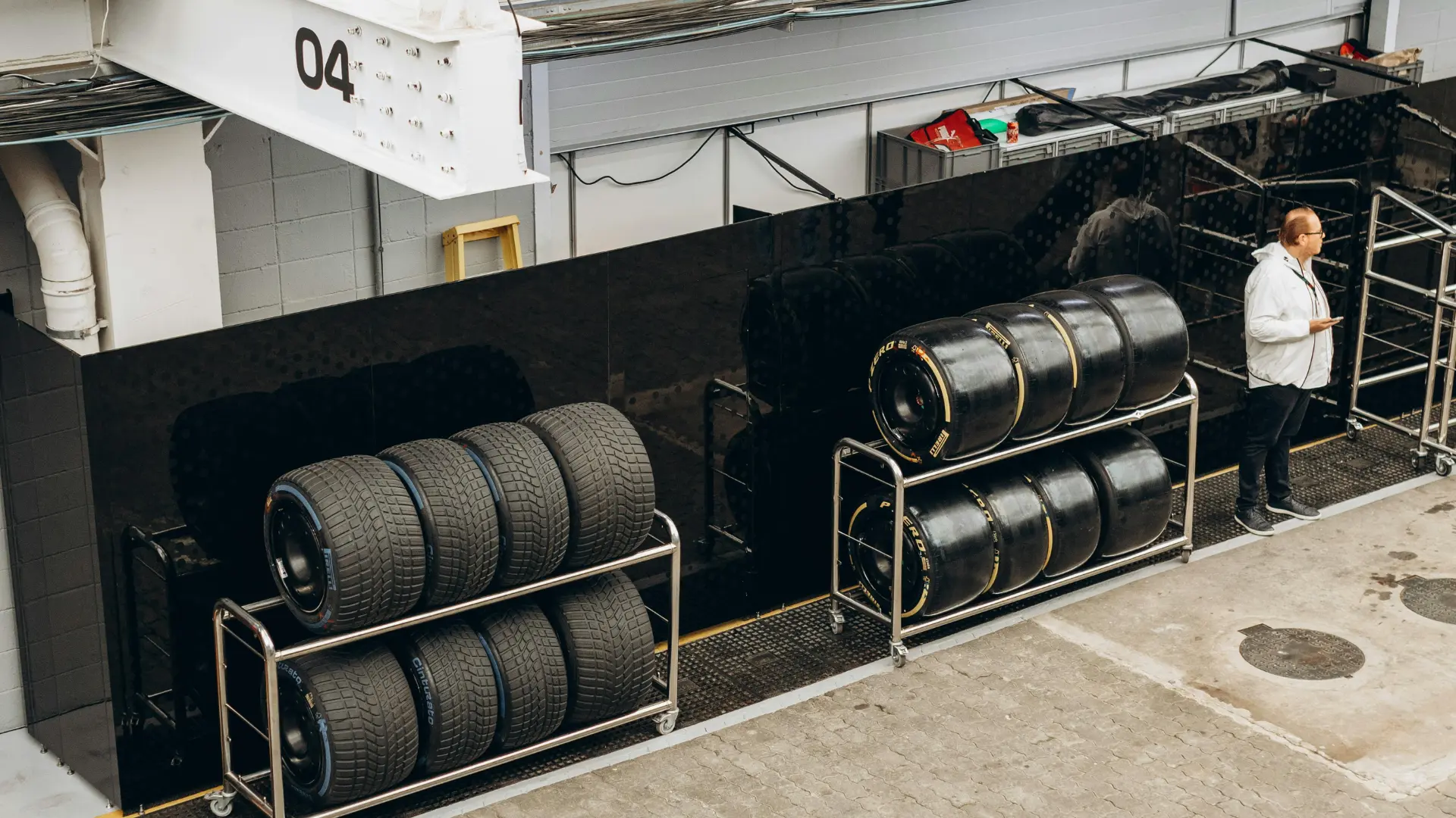 High-performance motorsport racing slick tires stacked on stainless steel rolling carts inside a professional racing pit lane garage.