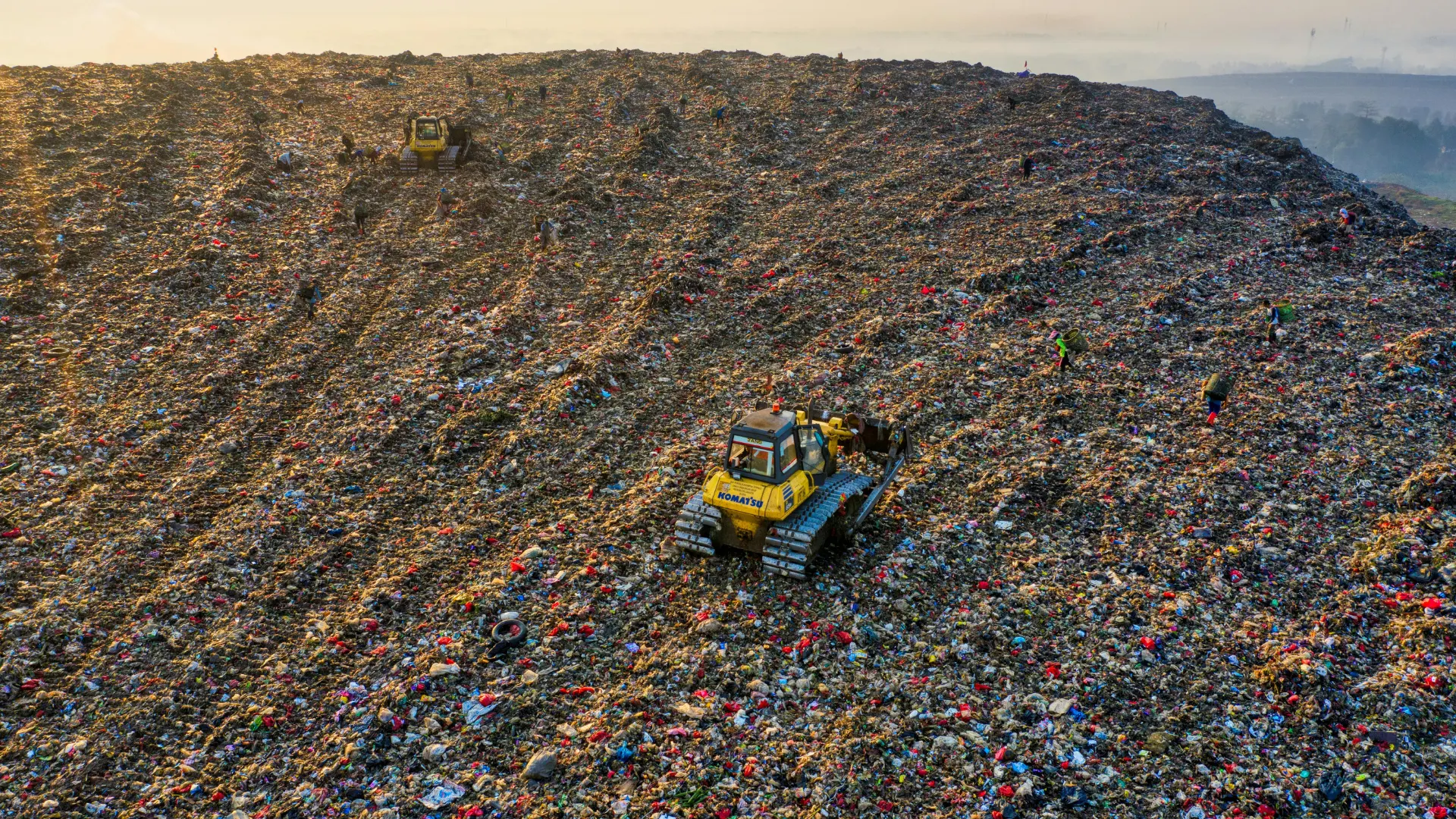 Aerial view of a massive municipal solid waste landfill with yellow bulldozers actively managing and compacting heavy garbage and debris.
