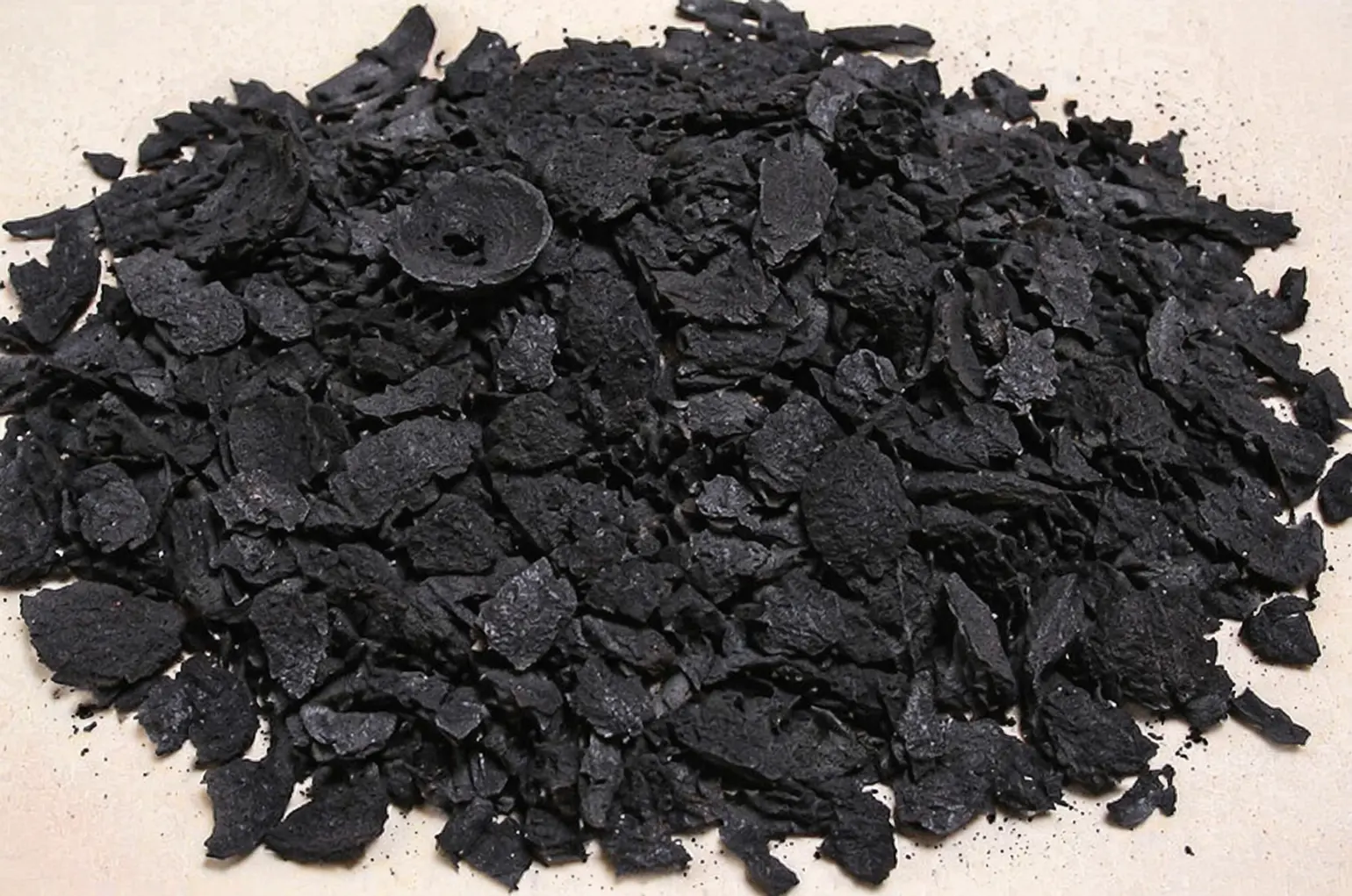 A close-up view of a bulk pile of raw, irregularly shaped coconut shell charcoal flakes, utilized as a high-quality precursor material for industrial activated carbon manufacturing and filtration systems.