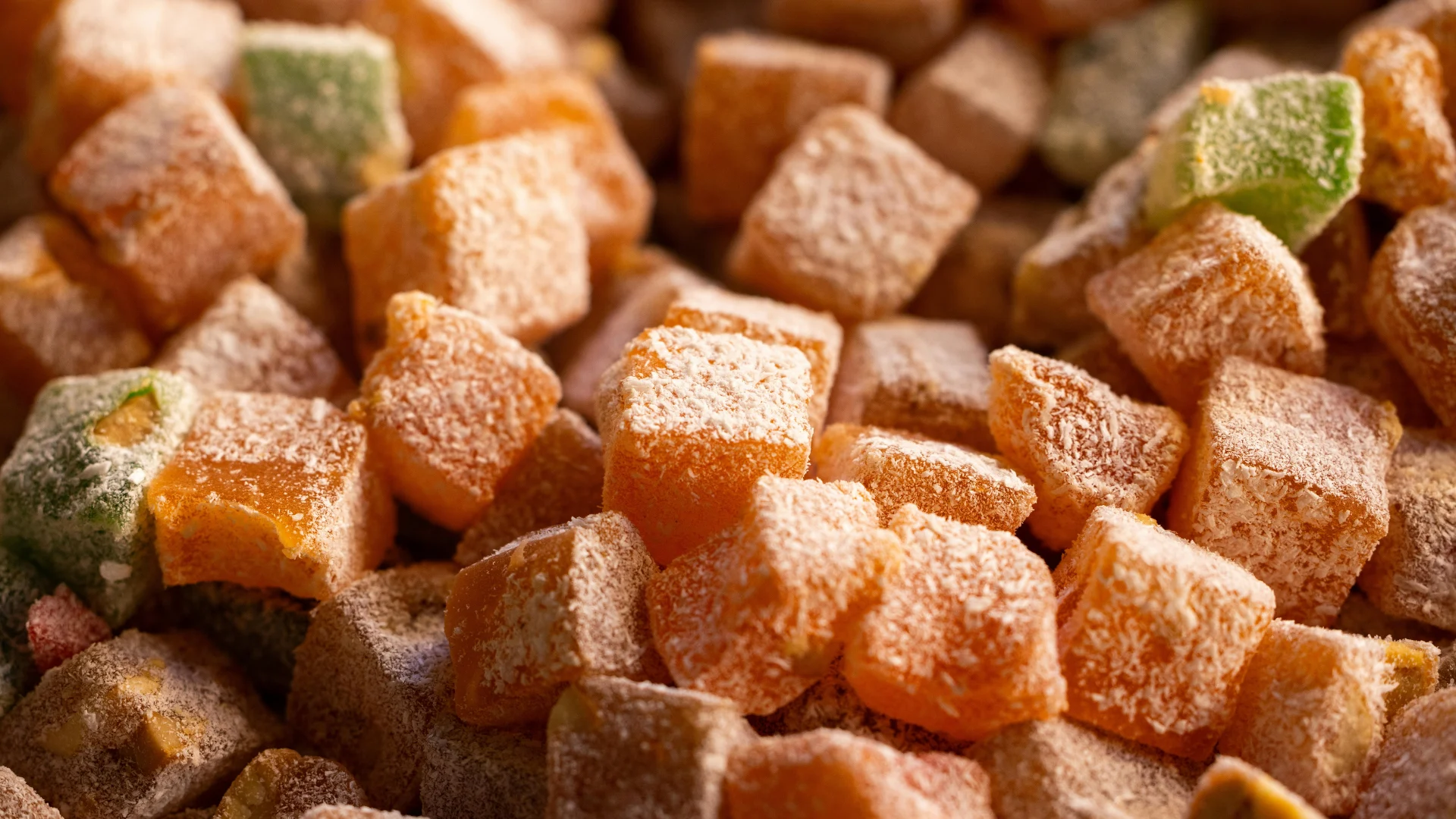 Macro photograph of colorful, traditional Turkish delight confectionery cubes generously dusted with powdered sugar and desiccated coconut.